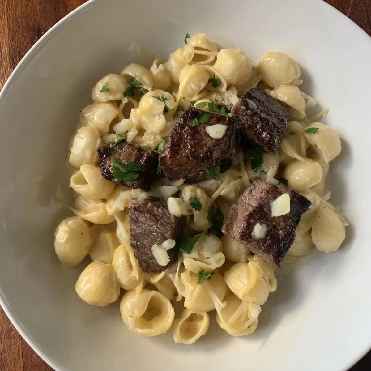 A close-up of tender garlic butter steak bites beside a serving of rich, decadent cheesy shells.