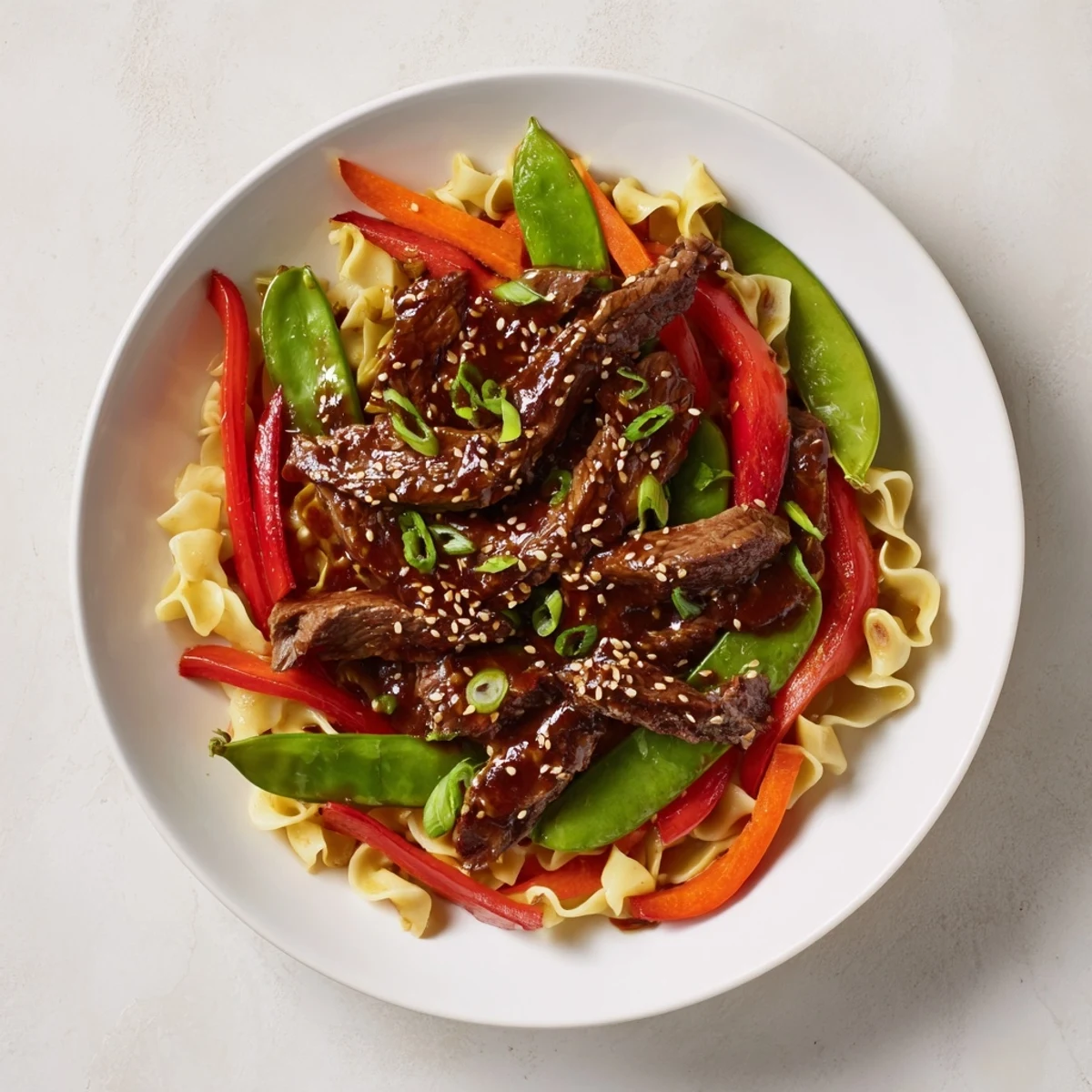 A close-up view of a flavorful Teriyaki Beef & Noodle Bowl, garnished with sesame seeds and green onions.