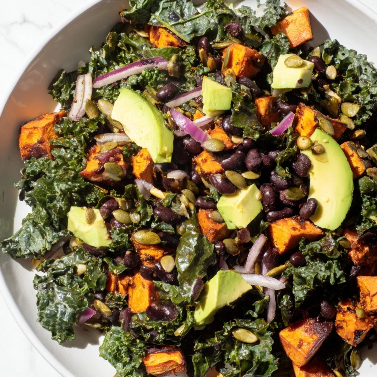 Vibrant massaged kale salad with warm sweet potato, black beans, and a zesty lime dressing.