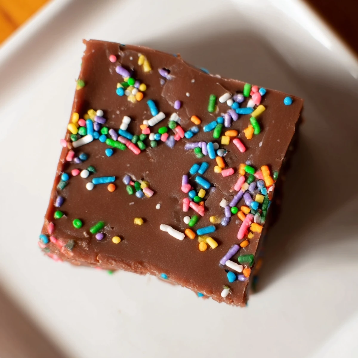Festive 3-Ingredient Christmas Fudge Squares glistens, topped with colorful sprinkles, awaiting a delicious bite.