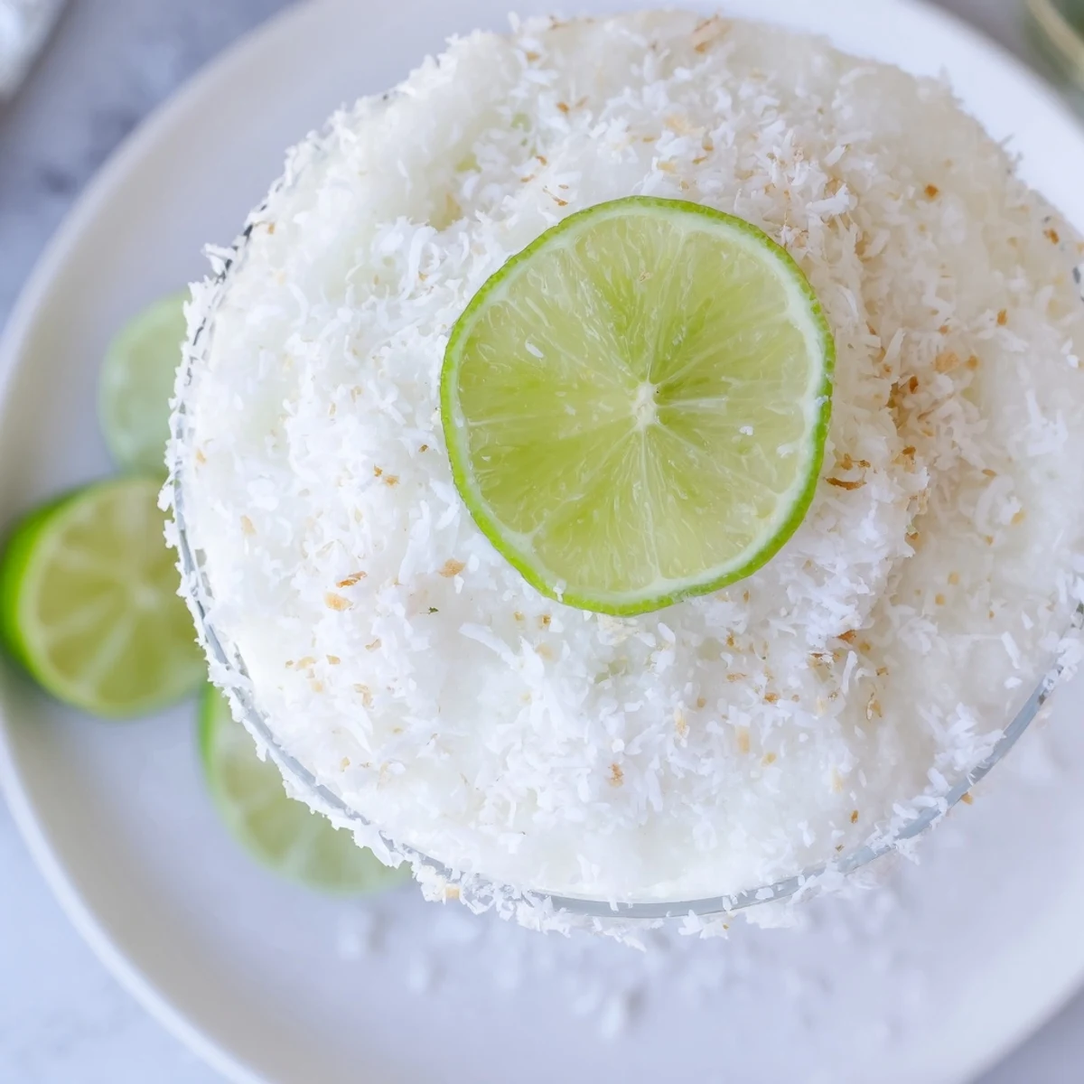 Frosted White Christmas Margarita slush, creamy, with lime wedges and coconut rim, ready to enjoy.