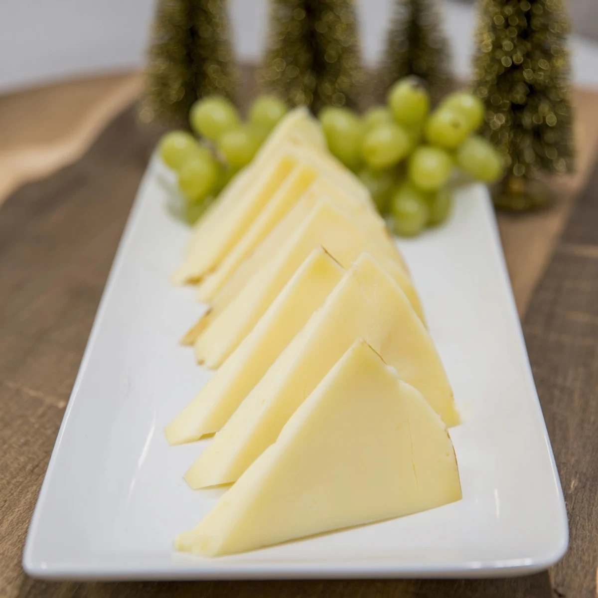 Festive The Tannenbaum Border cheese board with triangular cheese "trees" and vibrant green grapes.