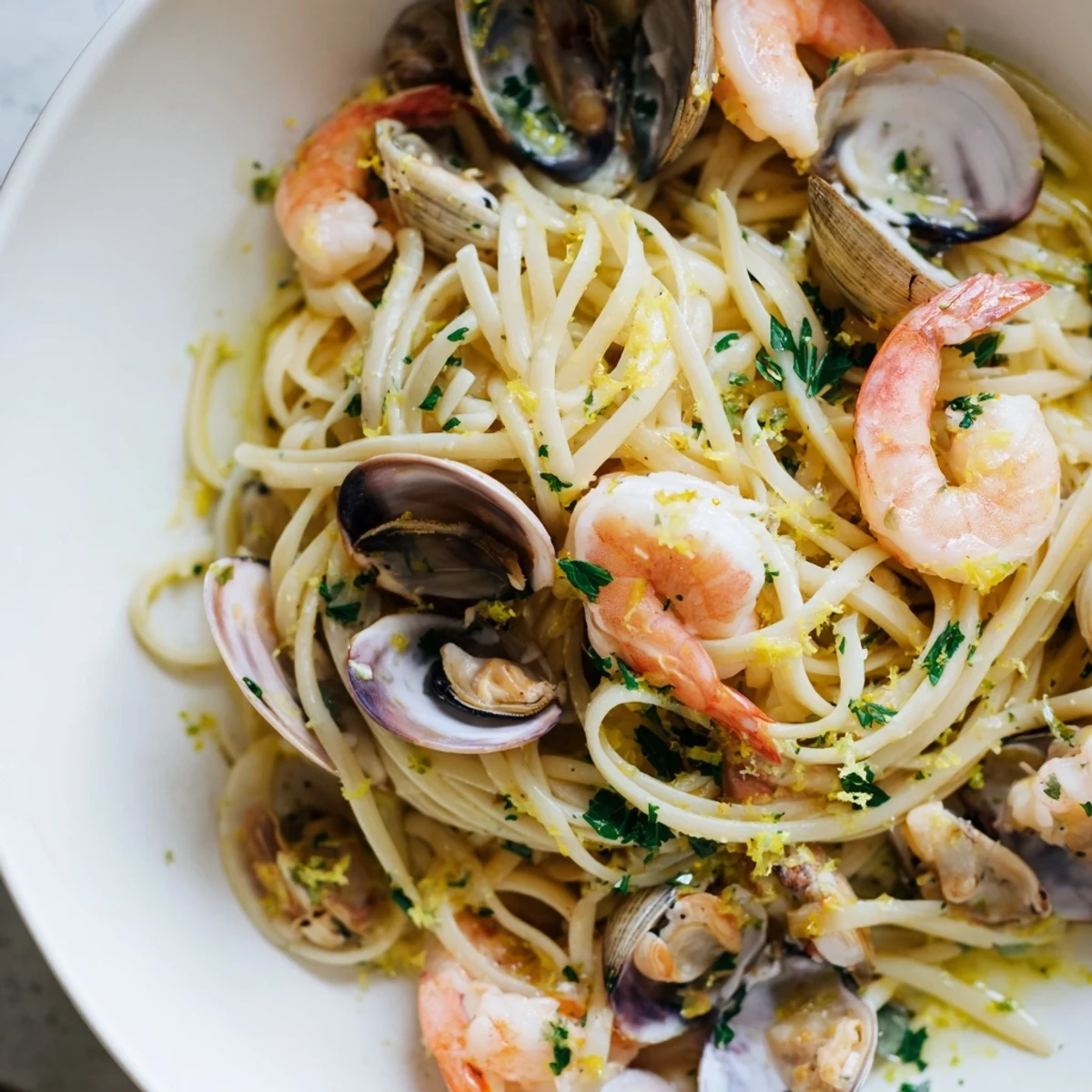 A close-up of Seafood Linguine with shrimp, clams, and mussels in a glossy white wine and garlic sauce, garnished with fresh parsley and lemon wedges.