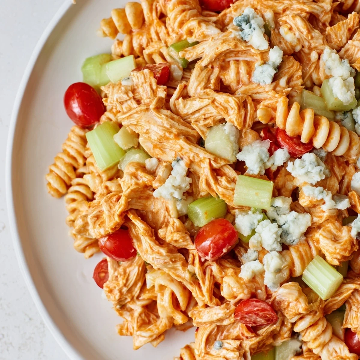 Bright bowl of Buffalo Chicken Pasta Salad featuring al dente rotini, crunchy veggies, and crumbled blue cheese garnish.