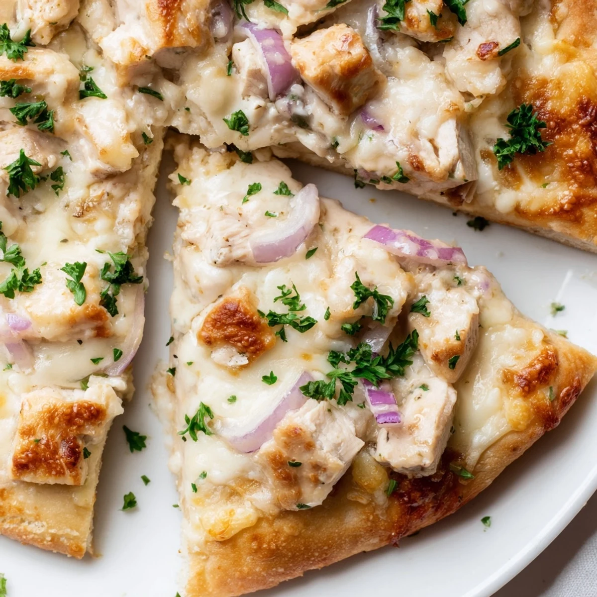 Freshly baked Chicken Alfredo Pizza cut into slices, revealing tender chicken and cheese layers, served on a wooden cutting board.