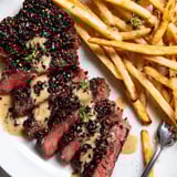 Savory classic peppercorn ribeye steak served alongside crispy golden fries on a plate.  