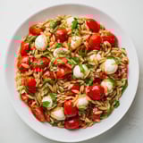 A vibrant bowl of Caprese Orzo Salad, ready to eat, with glistening tomatoes and creamy mozzarella.