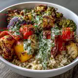 Hearty brown rice serves as the base for this vibrant Rainbow Roasted Vegetable Bowl, topped with zucchini, broccoli, and a drizzle of zesty lemon herb sauce.