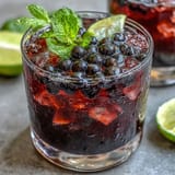 Close-up of a Black Currant Mojito featuring vibrant bubbles from club soda, a sprig of mint, and glistening condensation on the glass.