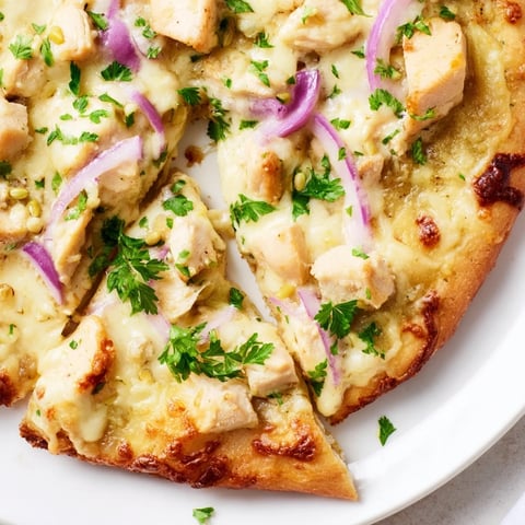 A close-up of golden-brown Chicken Alfredo Pizza, topped with creamy sauce, diced chicken, and melted mozzarella on a rustic crust.