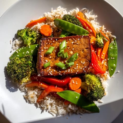 Crispy pan-seared tofu steaks, with colorful stir-fried vegetables, and rice are plated, ready to enjoy.
