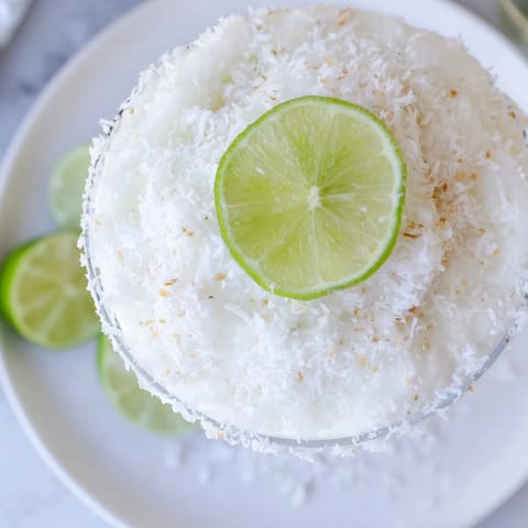 Frosted White Christmas Margarita slush, creamy, with lime wedges and coconut rim, ready to enjoy.