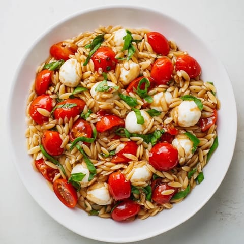 A vibrant bowl of Caprese Orzo Salad, ready to eat, with glistening tomatoes and creamy mozzarella.