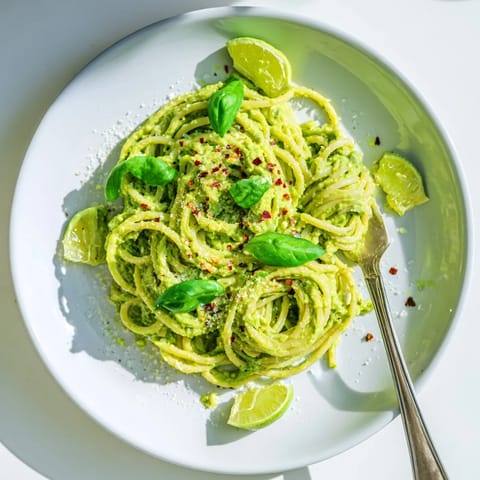 A vibrant bowl of avocado pasta topped with grated Parmesan and a lime wedge for a zesty finish.  