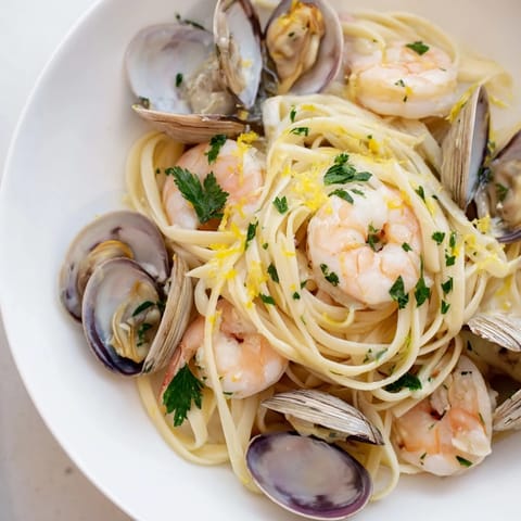 A rustic skillet of Seafood Linguine featuring plump shrimp and mussels, steaming in a fragrant lemon-garlic broth over al dente pasta.