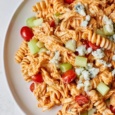 Bright bowl of Buffalo Chicken Pasta Salad featuring al dente rotini, crunchy veggies, and crumbled blue cheese garnish.