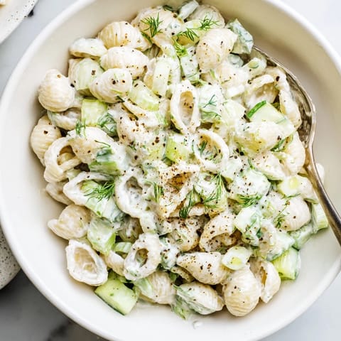 A chilled bowl of Cucumber Crunch Pasta Salad ready for a summer picnic, featuring bright greens, savory seasoning, and a tangy, creamy finish.  