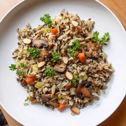 A close-up of fluffy wild rice pilaf mixed with sautéed mushrooms, carrots, and celery, ready for a family dinner.