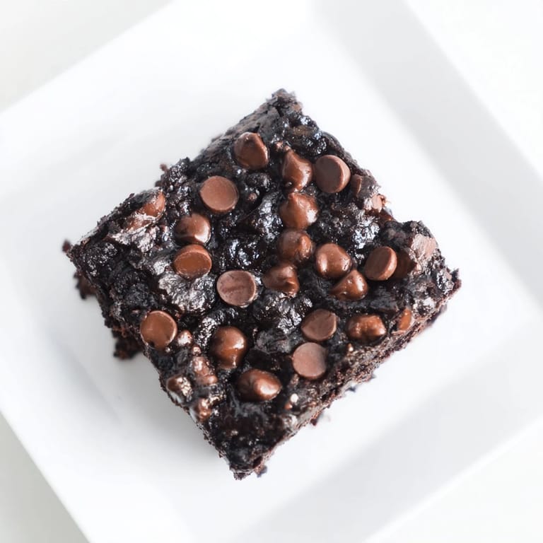 A warm plate of baked Black Bean Brownies, showcasing a soft, brownie center and sprinkled chocolate chips on top.