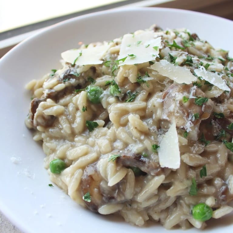 Orzo Mushroom Risotto-Style served on a white plate, garnished with fresh herbs and grated Parmesan.