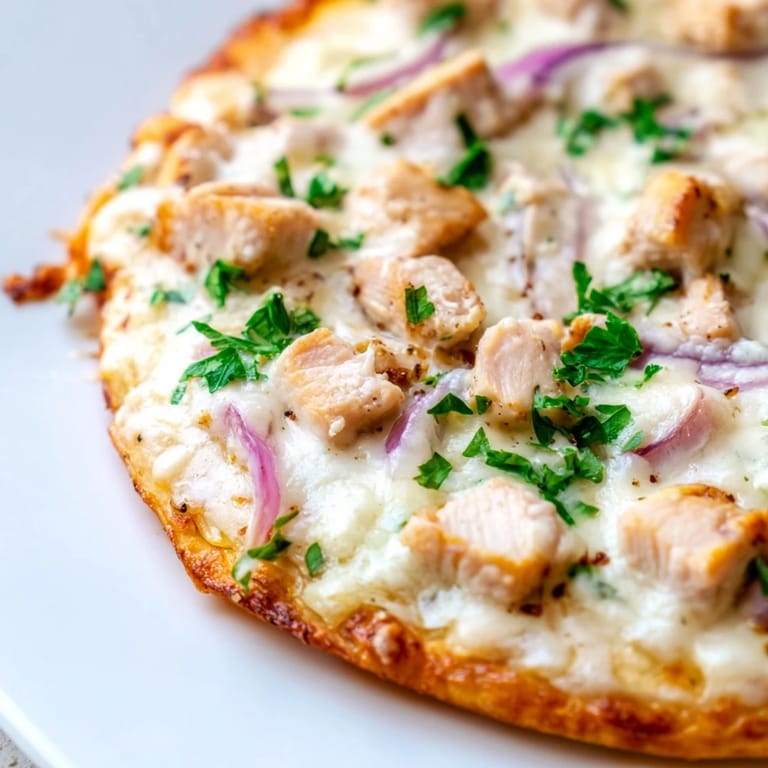 A slice of Chicken Alfredo Pizza being lifted, showcasing gooey cheese and a rich white sauce over a perfectly baked crust.