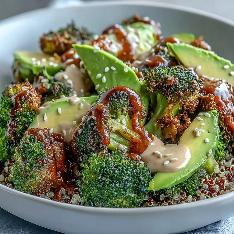 A close-up of a colorful Roasted Broccoli Bowl showing a forkful of crispy broccoli and fluffy quinoa dipped in creamy tahini sauce. Fresh avocado and lemon slices add a vibrant finish to this healthy vegetarian meal.