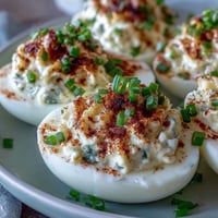 Freshly made Million Dollar Deviled Eggs garnished with paprika and chives, ready to serve chilled.