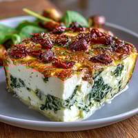A golden, oven-baked frittata with vibrant spinach, creamy feta, and tangy sun-dried tomatoes, perfect for brunch or dinner.